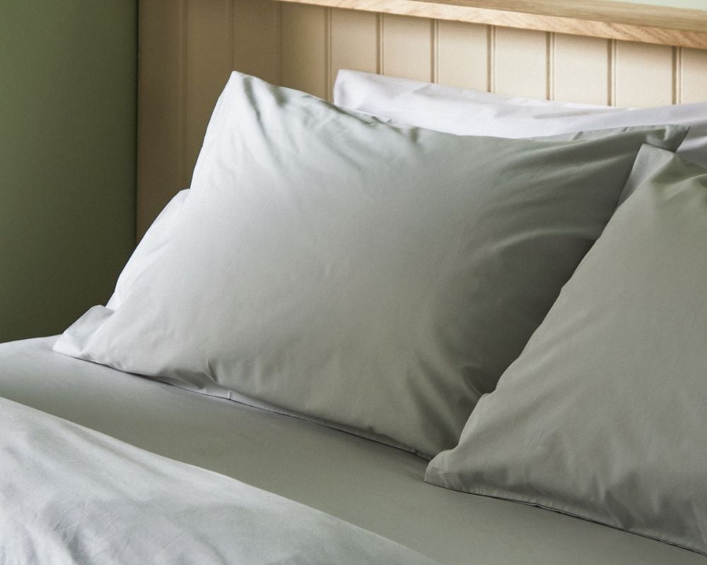 Two light gray pillows on a bed with a wooden headboard.