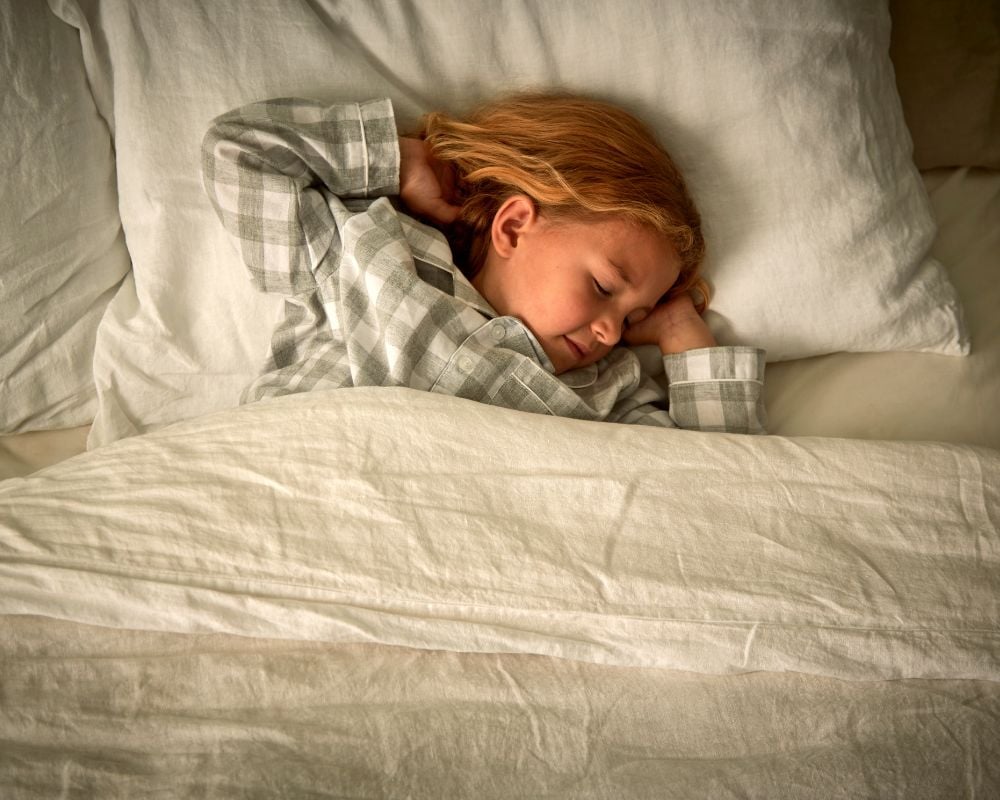 Child sleeping under a blanket on a bed with pillows