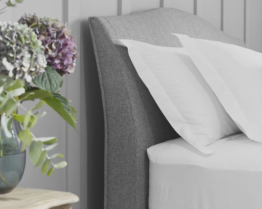 Gray upholstered headboard with white pillows and a vase of flowers on a wooden surface.