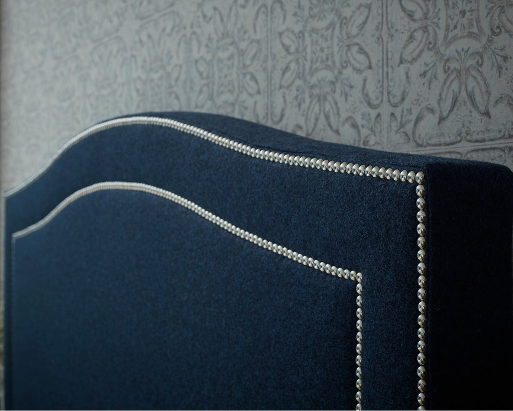Navy blue upholstered headboard with silver nailhead trim against a patterned wall.