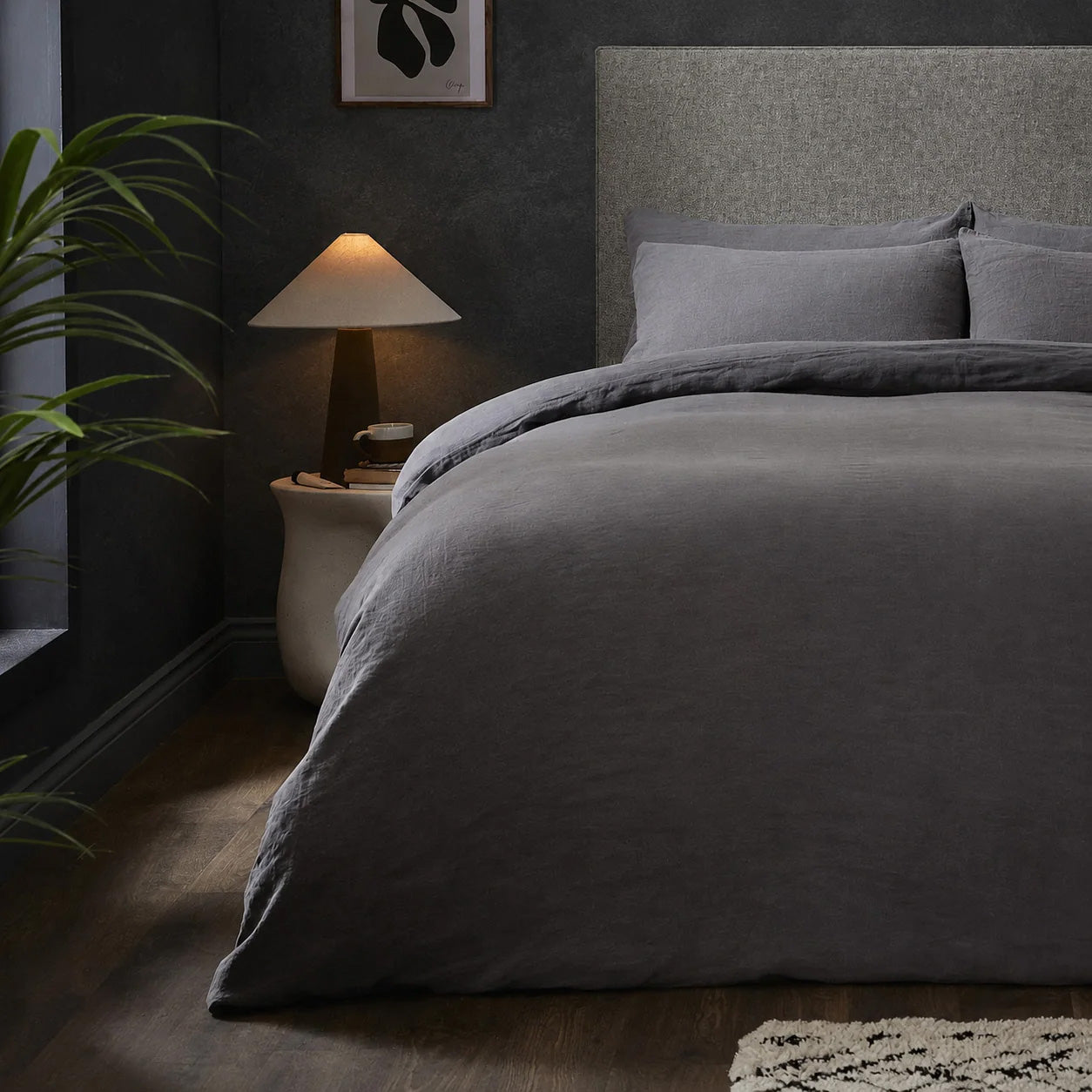 A dressed bed with Woolroom's Mariana Linen Comforter Cover in Charcoal has the comforter turned down and two pillows. 