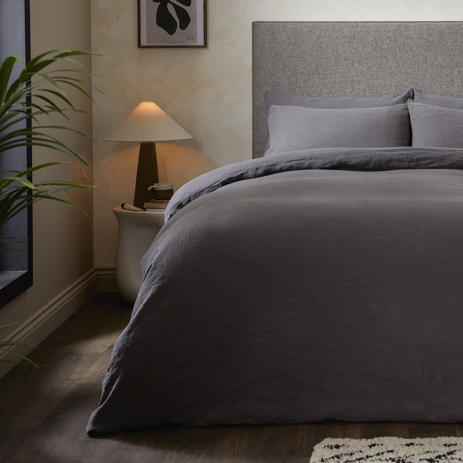 A dressed bed with Woolroom's Mariana Linen Comforter Cover in Charcoal has the comforter turned down and two pillows. 