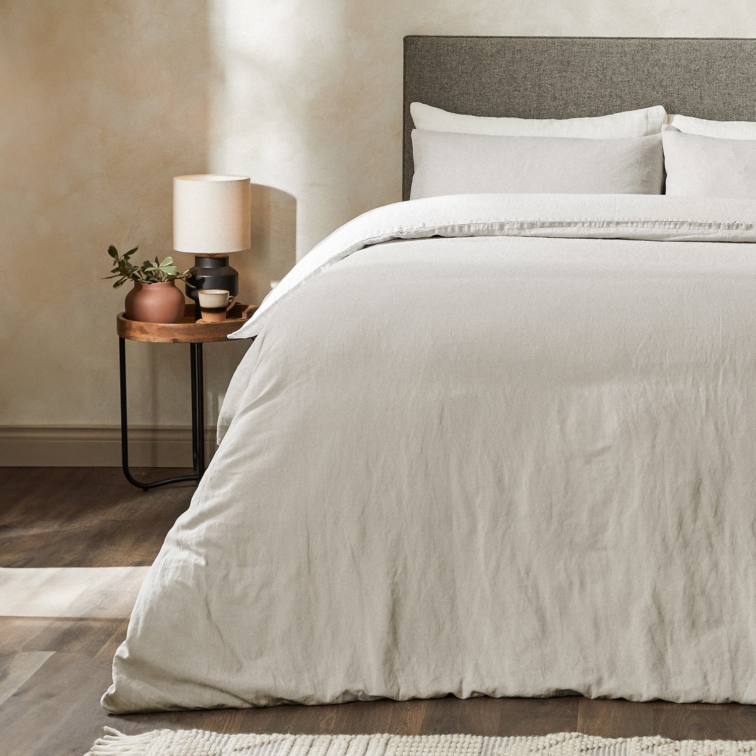A dressed bed with Woolroom's Mariana Linen Comforter Cover in Pebble has the comforter turned down and two pillows. 