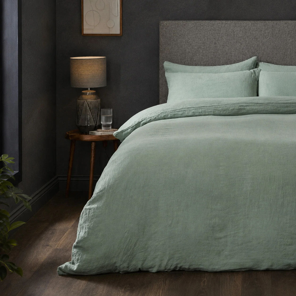 A dressed bed with Woolroom's Mariana Linen Comforter Cover in Sage has the comforter turned down and two pillows. 
