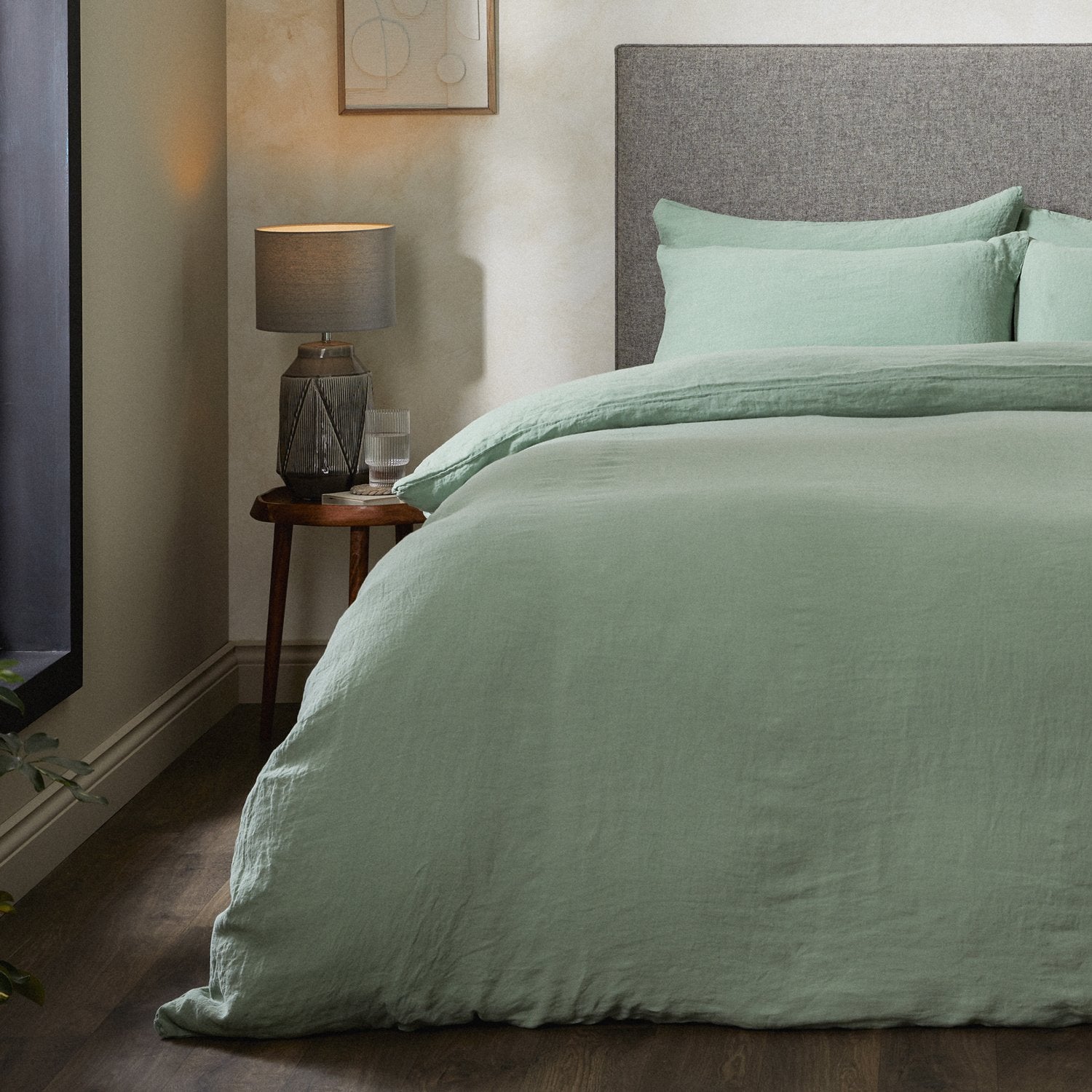 A dressed bed with Woolroom's Mariana Linen Comforter Cover in Sage has the comforter turned down and two pillows. 