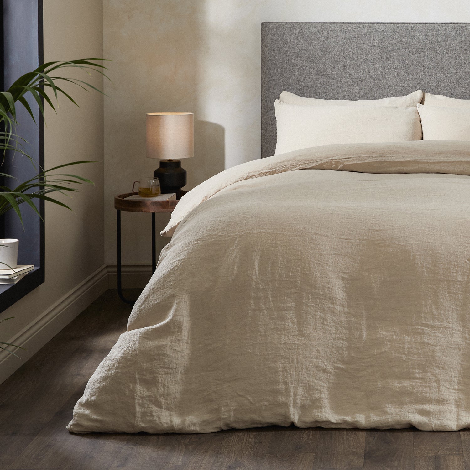 A dressed bed with Woolroom's Mariana Linen Comforter Cover in Sand has the comforter turned down and two pillows. 