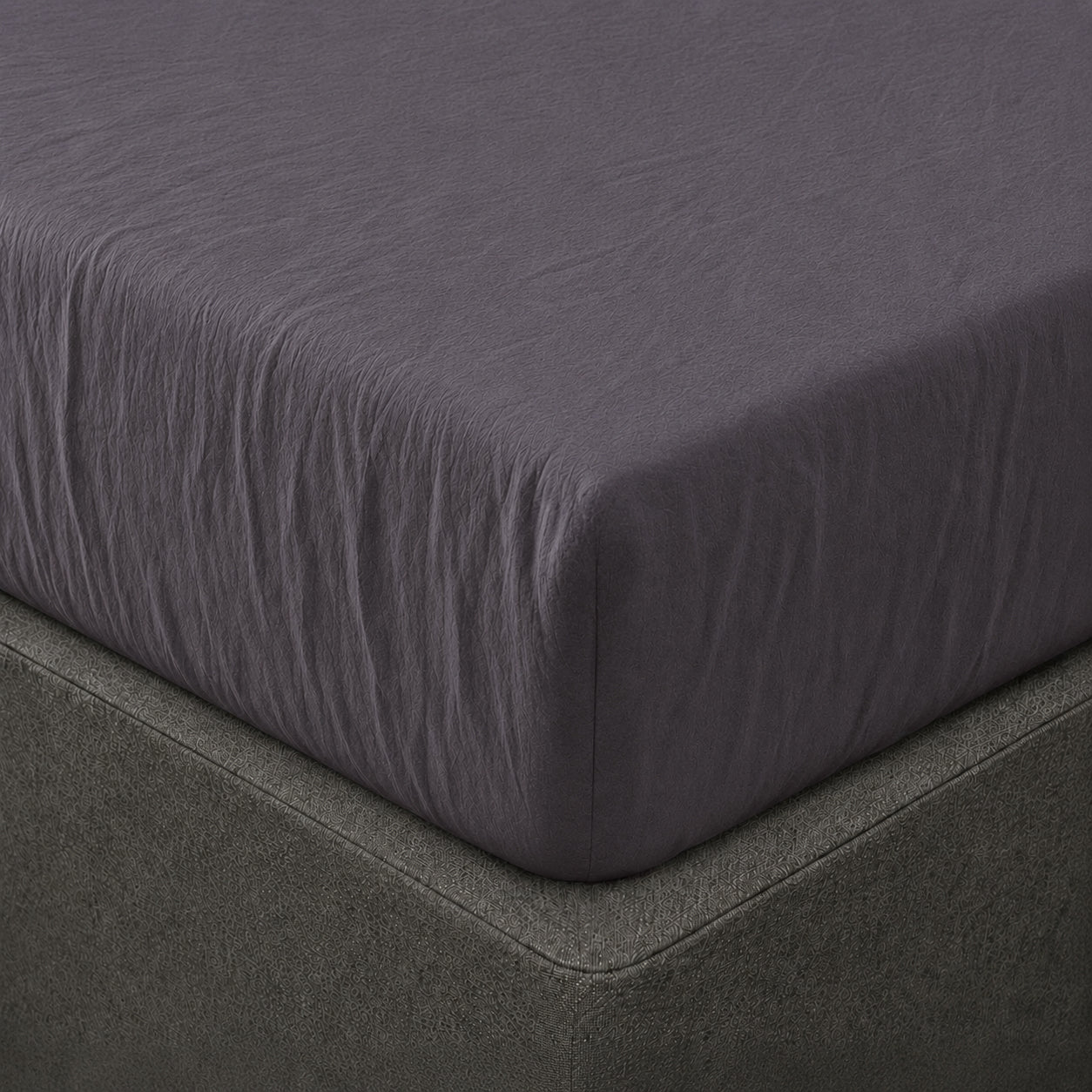 A close up of the corner of a mattress with Woolroom's Mariana Linen Blend Fitted Sheet in Charcoal.
