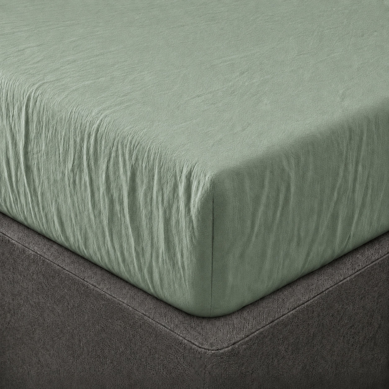 A close up of the corner of a mattress with Woolroom's Mariana Linen Blend Fitted Sheet in Sage.