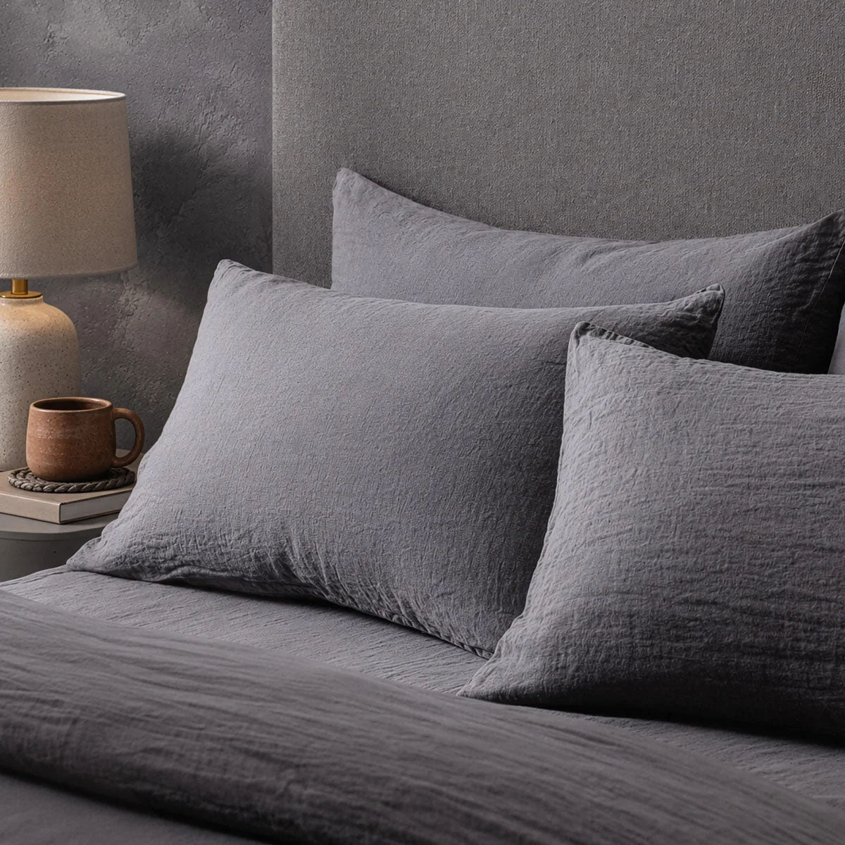 Four pillows on a dressed bed with the Mariana Linen Blend Pillow Cases in Charcoal.