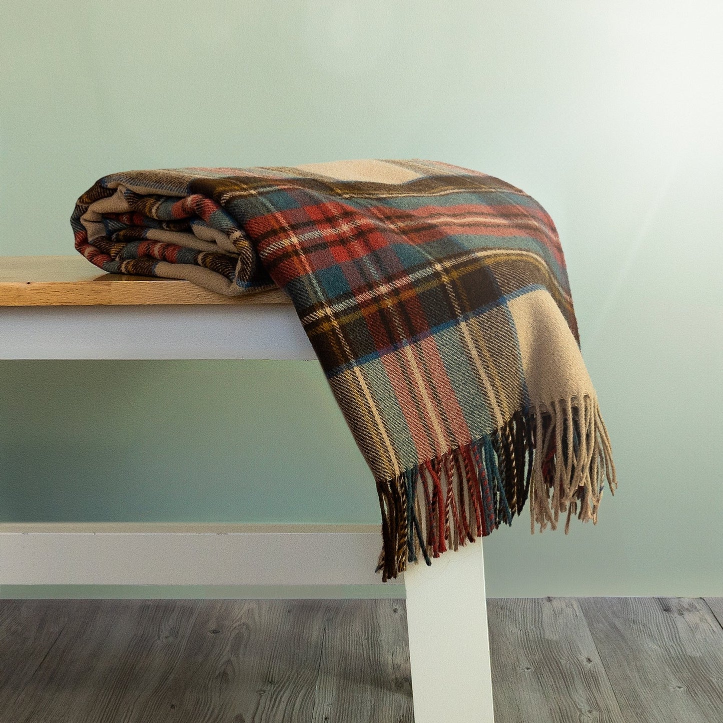 The Antique Dress Stewart Tartan Throw in Orange and Brown is rolled and hanging over the edge of a bench showing the fringe. 
