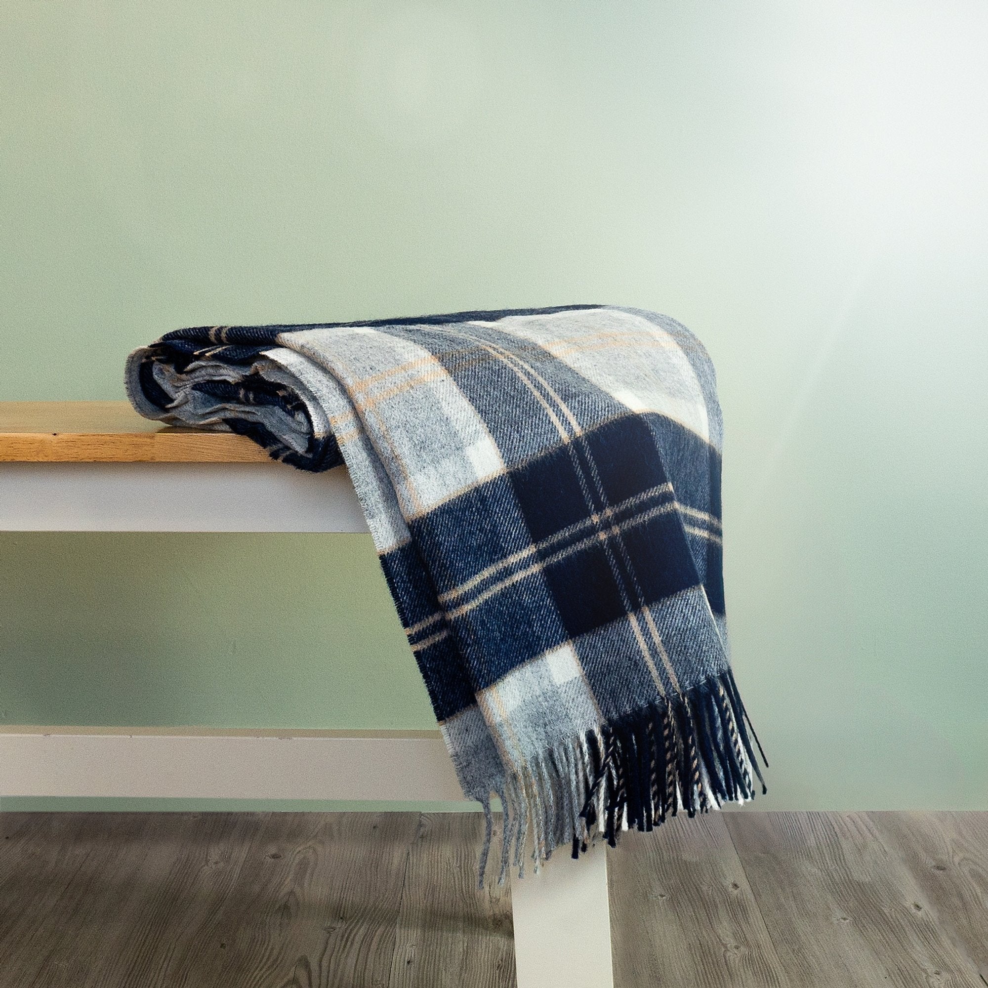 The Bannockbane Tartan Throw in Silver and Blue is rolled and hanging over the edge of a bench showing the fringe. 