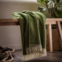 The beautifully soft Herringbone Shetland Wool Throw in color Apple green with white fringe, draped over a bench. 