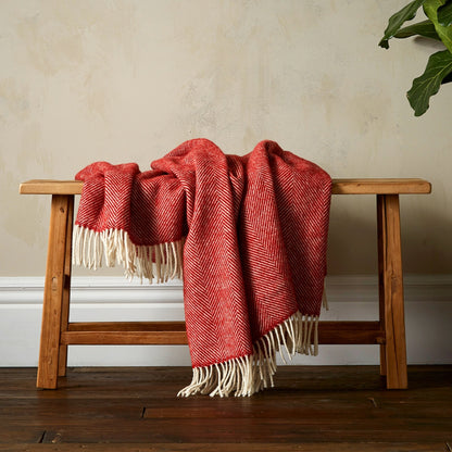 The super soft Greta Herringbone Wool Blanket in Terracotta draped over a bench with white fringe. 