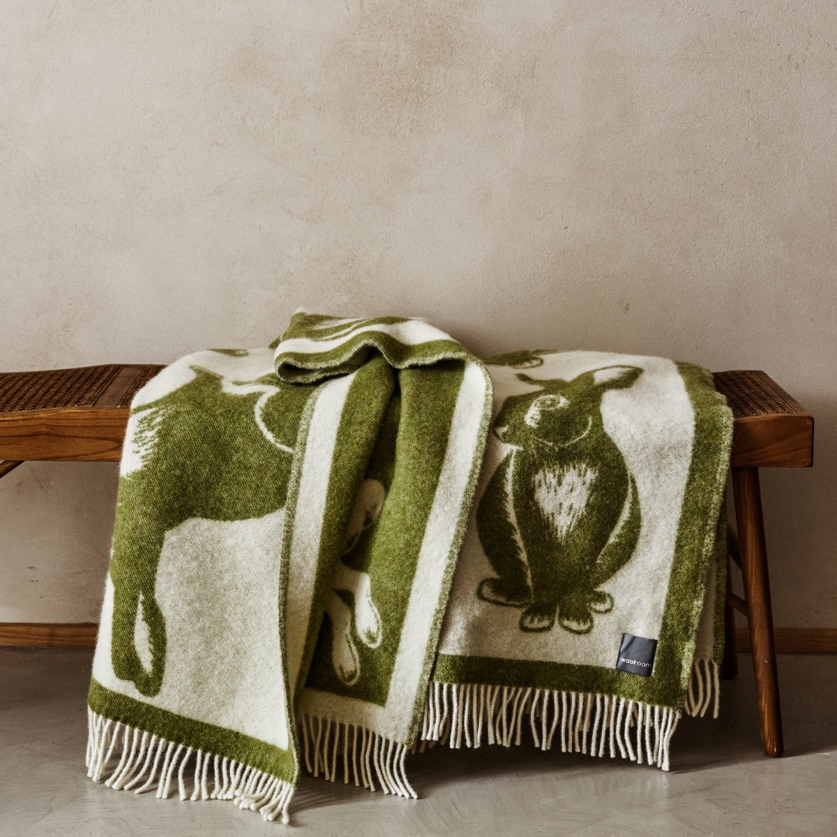 The playful Wild and Wool Rabbit Wool Throw in Moss with white fringe belongs to the Woolroom animal throw collection.