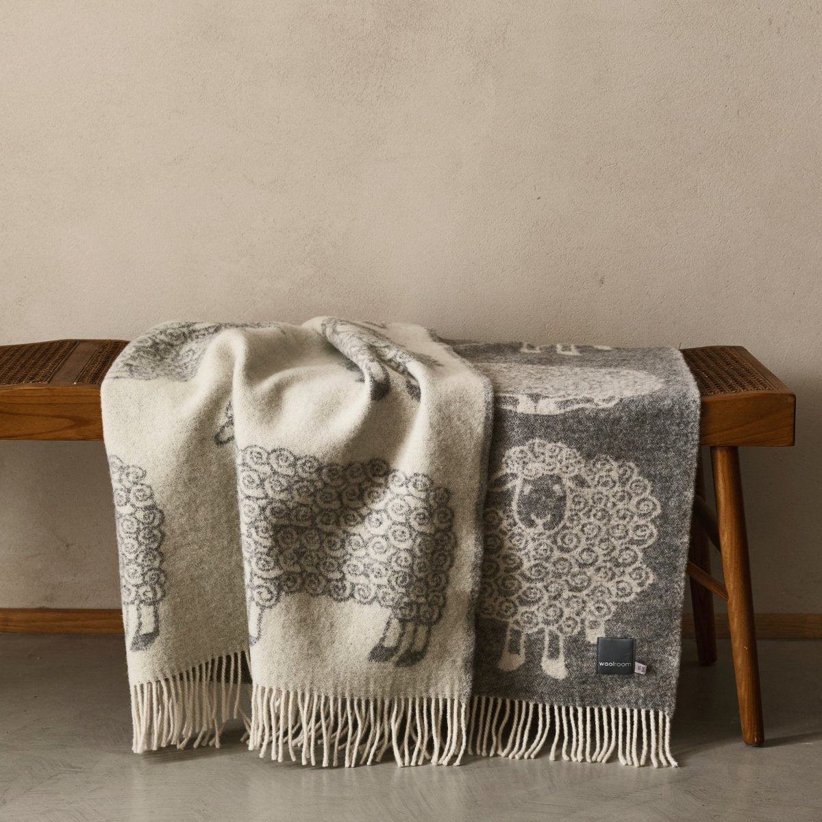The playful Wild and Wool Lamb Wool Throw in Stone with white fringe belongs to the Woolroom animal throw collection.