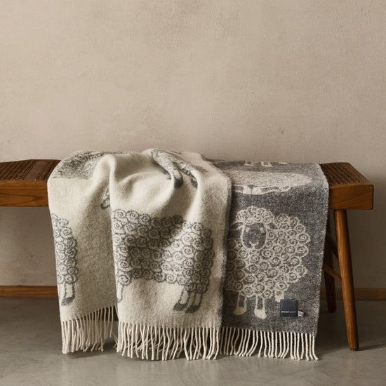 The playful Wild and Wool Lamb Wool Throw in Stone with white fringe belongs to the Woolroom animal throw collection.