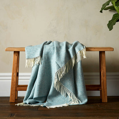 The Herringbone Shetland Throw in color Duck Egg with white fringe, draped over a bench. 