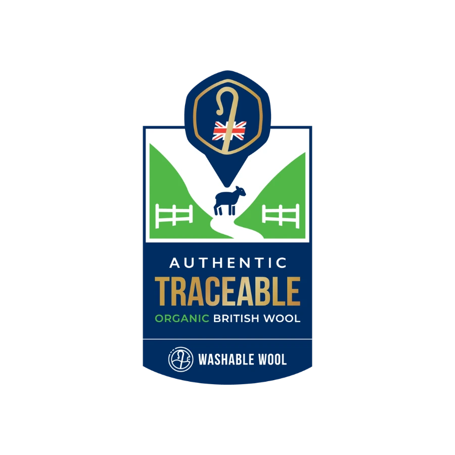 A brand logo for 'Washable Wool' featuring a shield design with a blue background, green hills, a black sheep silhouette, and a gold shepherd's crook icon with a Union Jack flag. Text on the logo reads 'Authentic Traceable Organic British Wool' and 'Washable Wool'.