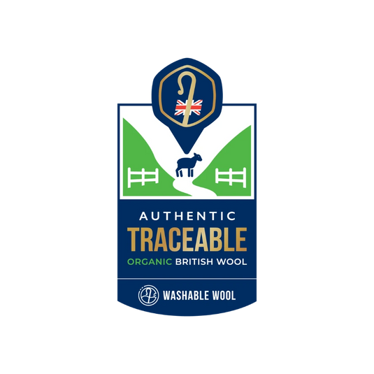 A brand logo for 'Washable Wool' featuring a shield design with a blue background, green hills, a black sheep silhouette, and a gold shepherd's crook icon with a Union Jack flag. Text on the logo reads 'Authentic Traceable Organic British Wool' and 'Washable Wool'.