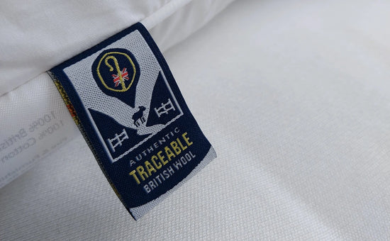 Close-up of a white woven textile with a sewn fabric label reading 'AUTHENTIC TRACEABLE BRITISH WOOL' and a crest-style logo, showing the material texture and label details.