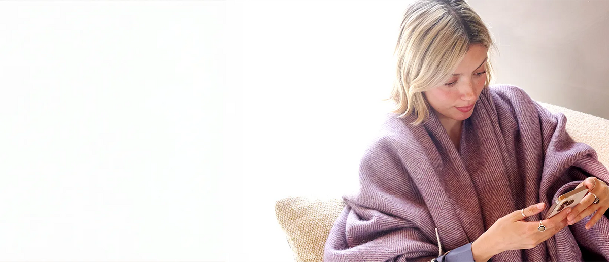 Woman wrapped in a pink blanket using a smartphone on a white background