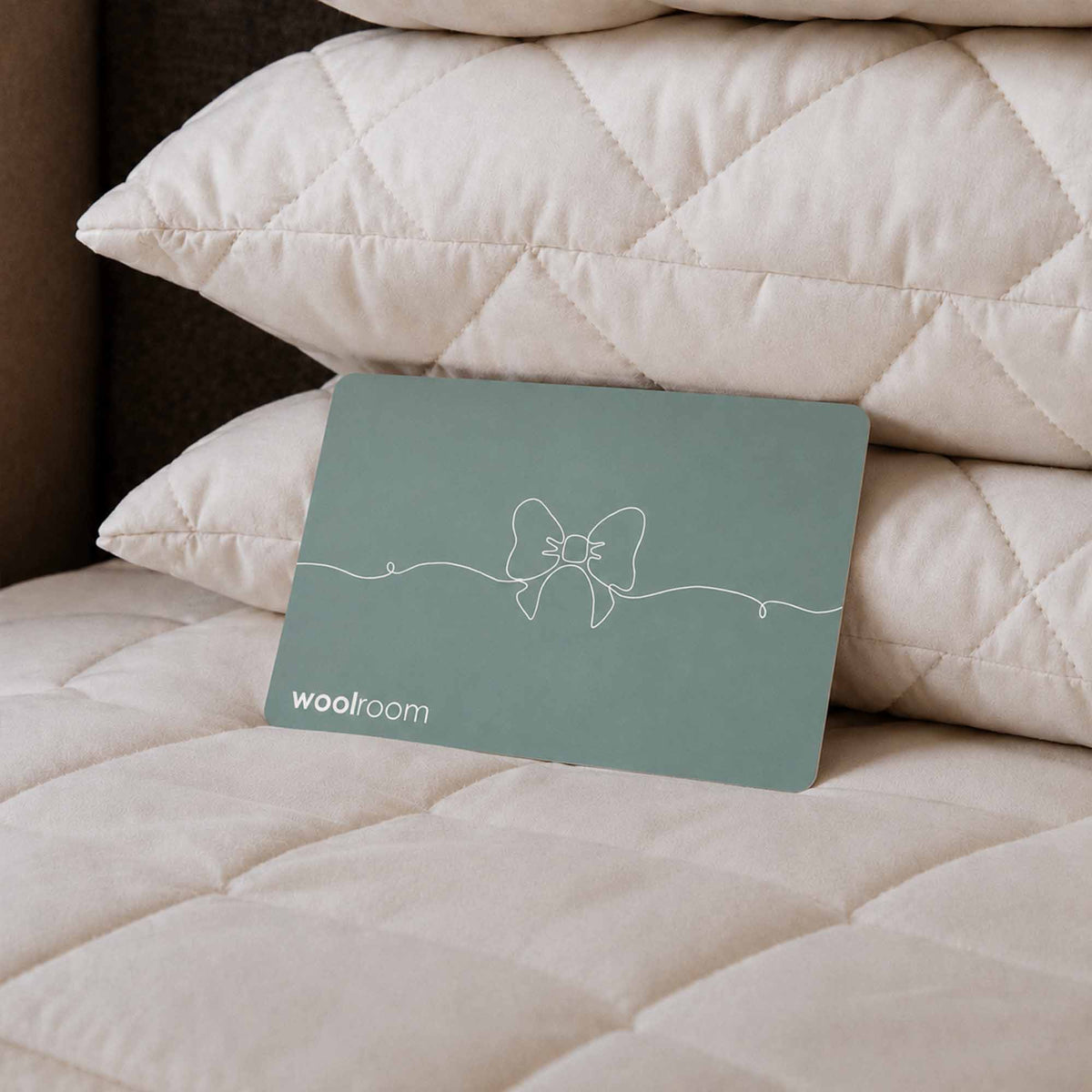 Teal gift card from the Woolroom on natural wool bedding and pillows.