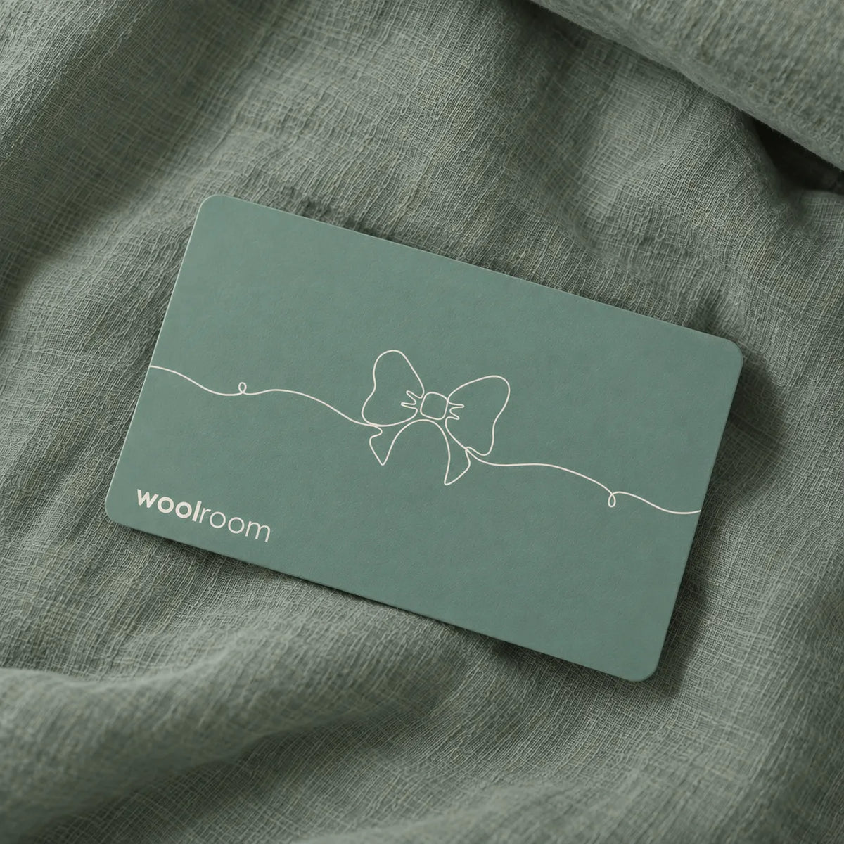 Teal coloured gift card for the wooloom on green linen bedding.