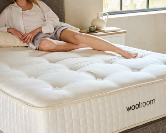 Person sitting on a woolroom mattress in a bedroom setting