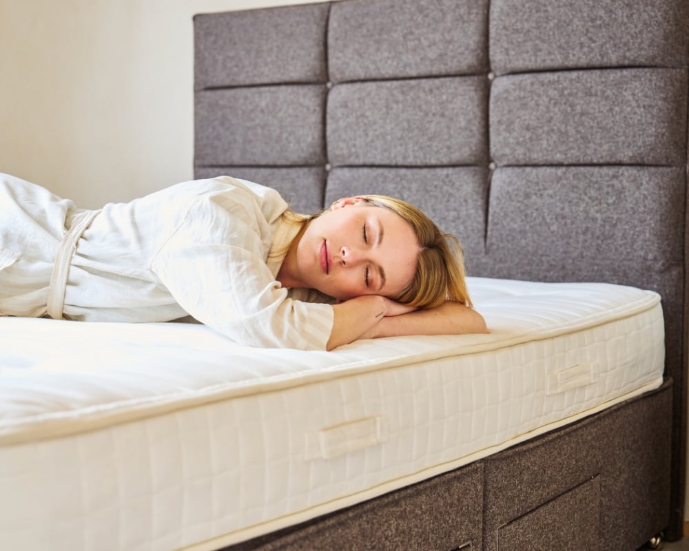 Woman lying on a mattress with a gray upholstered headboard