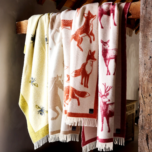 A collection of blue, green, red, beige and yellow wool throws draped over a wooden banister in a home.