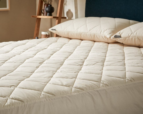Beige quilted mattress topper on a bed with pillows in a bedroom setting.