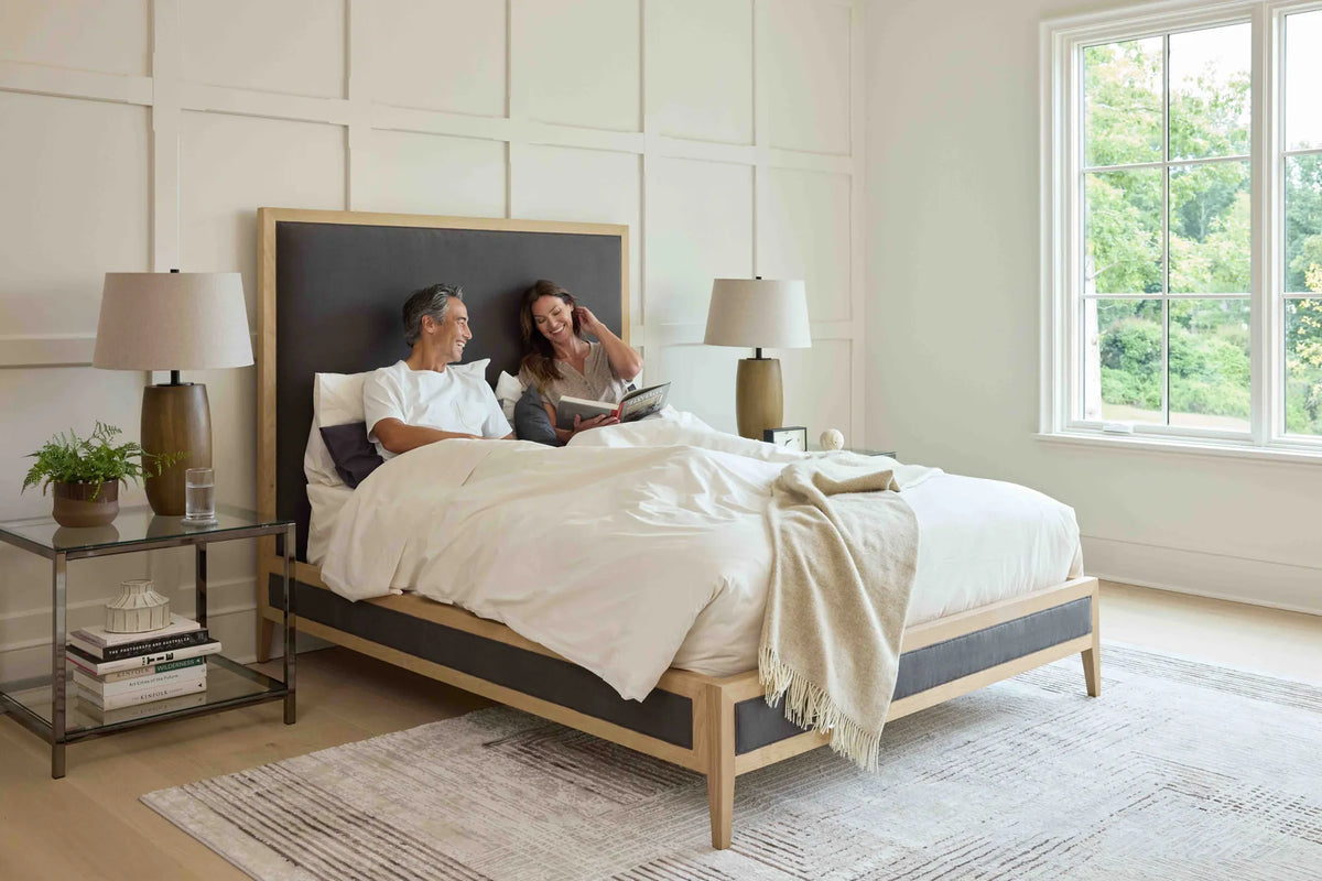 Couple reading in bed on the Victoria bed frame with white oak and charcoal upholstery